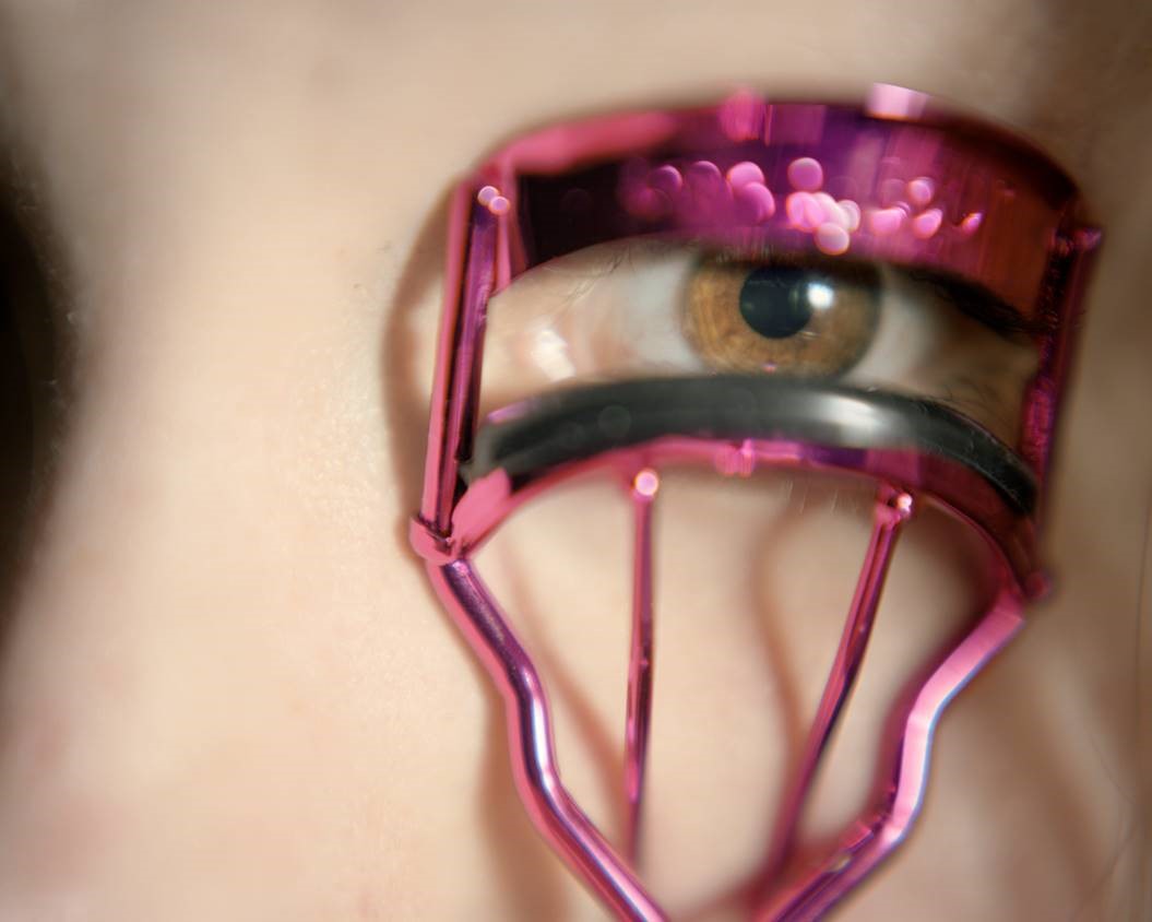 Image of girls eye with pink eyelash curler being used to curler lashes