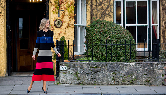 Woman dressed fashionably in a stripey knit dress outside a yellow building in Adare, Co. Limerick