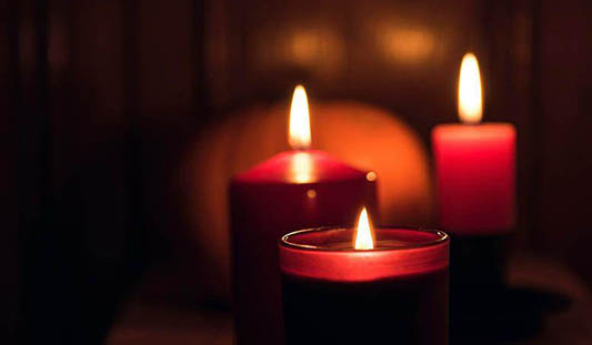 Three red lit candles in the dark with a pumpkin in the background. Photo: Joanna Kosinska / Unsplash