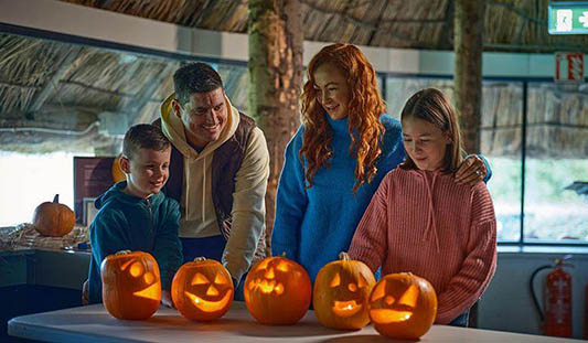 Family of four standing in front of 4 jack-o-lanterns on a table in Lough Gur Visitor Centre, Co. Limerick. Photo: Ireland's Content Pool