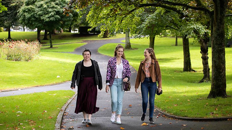 three young women walking in a green park area